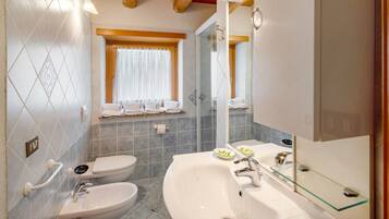 Ein Badezimmer mit weißem Waschbecken, einem Bidet, einer Toilette, einer Duschkabine aus Glas und einem Fenster mit Vorhängen.