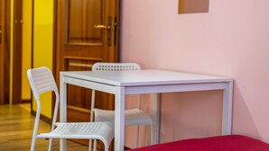 Ein Zimmer mit einem weißen Tisch, zwei weißen Stühlen, einem roten Bett und Holztüren.