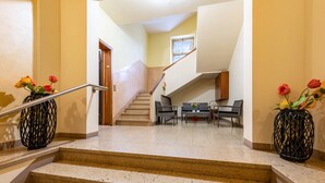 Un escalier avec une rampe, un coin repas avec une table et des chaises, et deux vases avec des fleurs.