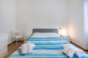 Una habitación de hotel con una cama, dos mesitas de noche, una silla y una lámpara.