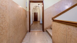 Un couloir au sol en marbre, avec une rambarde en bois et une porte au fond.