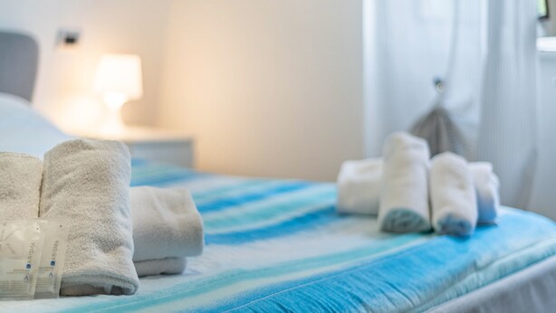 Un lit avec des serviettes, une lampe de chevet et une fenêtre avec des rideaux.
