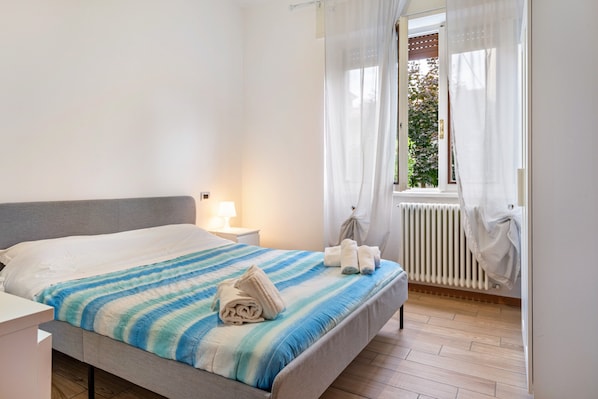 Un dormitorio con cama, mesita de noche y ventana con cortinas.