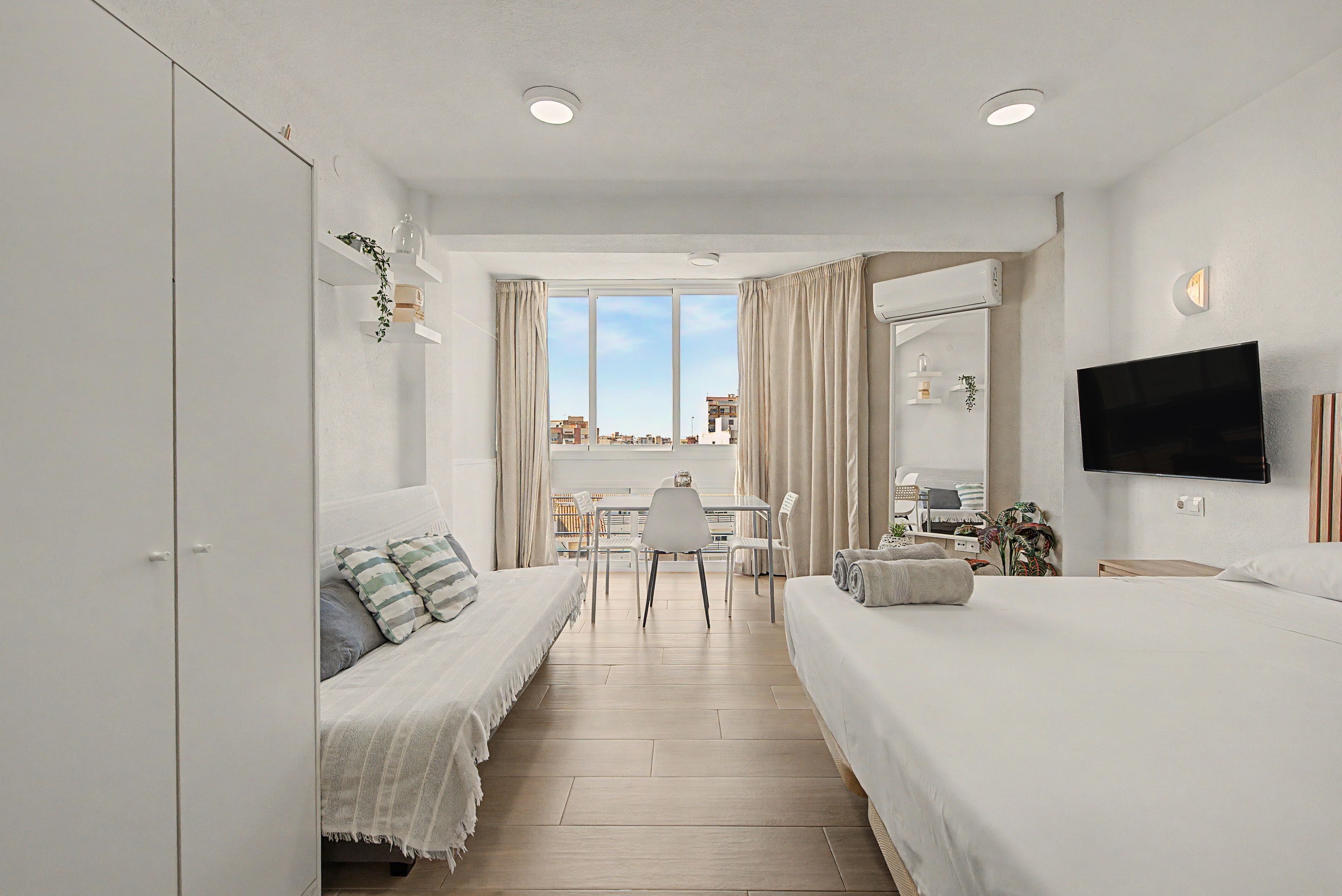 Habitación de hotel con cama, sofá, televisión, escritorio y vista a la ciudad.