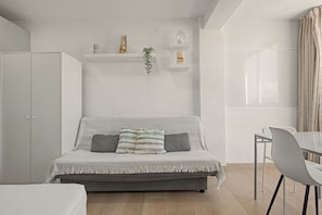 Ein modernes Schlafzimmer mit einer grauen Couch, einem kleinen Tisch und einem weißen Kleiderschrank.