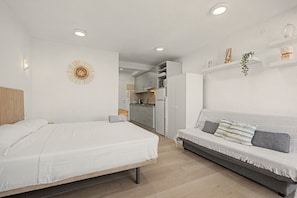 A modern bedroom with a bed, a sofa, a kitchen area, and a dining table.