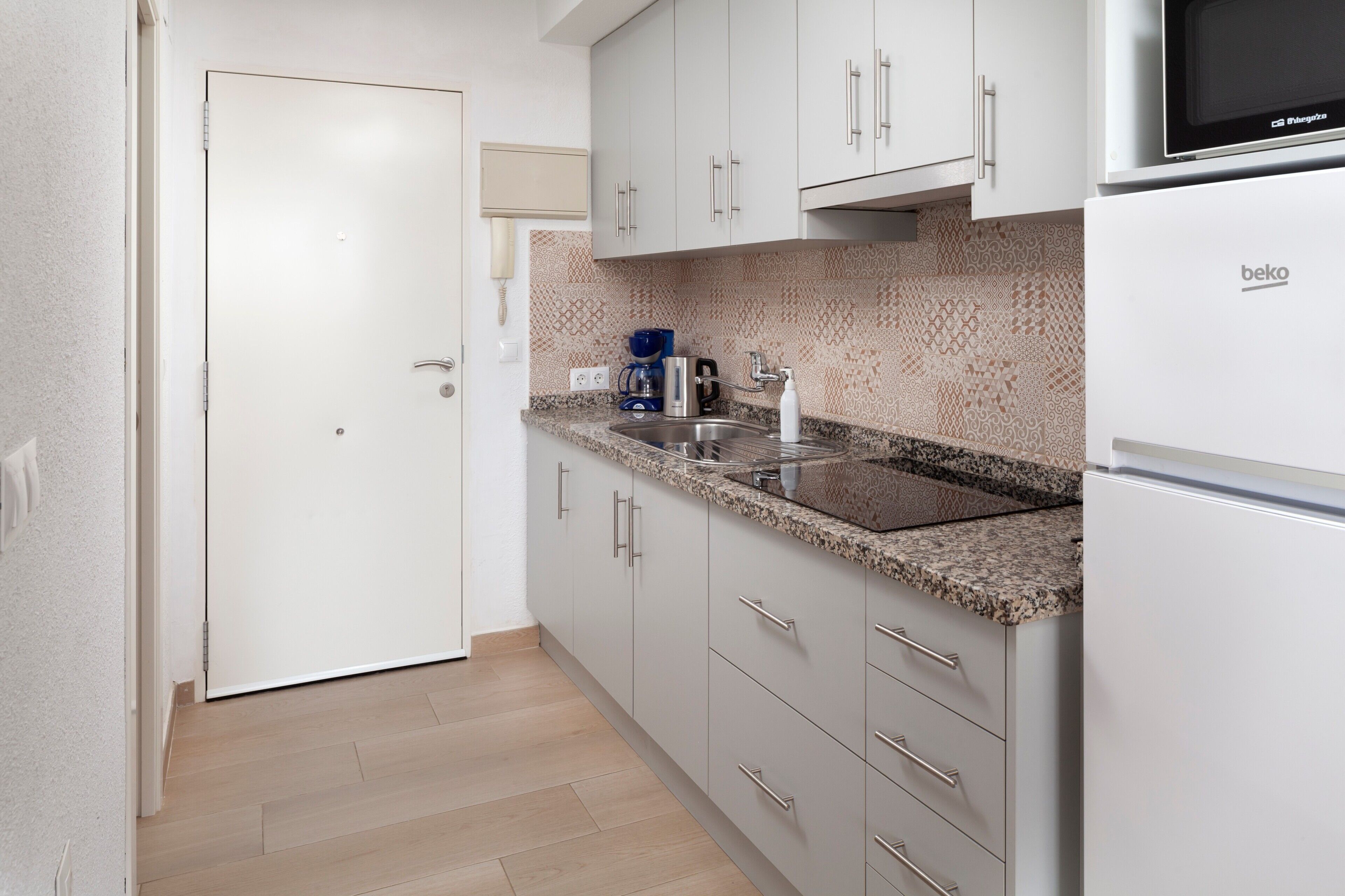 Una cocina con armarios blancos, encimera de granito, microondas y refrigerador.