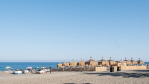 Une plage avec des parasols en chaume, des bateaux et un ciel dégagé.