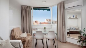 Un salon moderne avec un coin repas, de grandes fenêtres et une vue sur les immeubles.