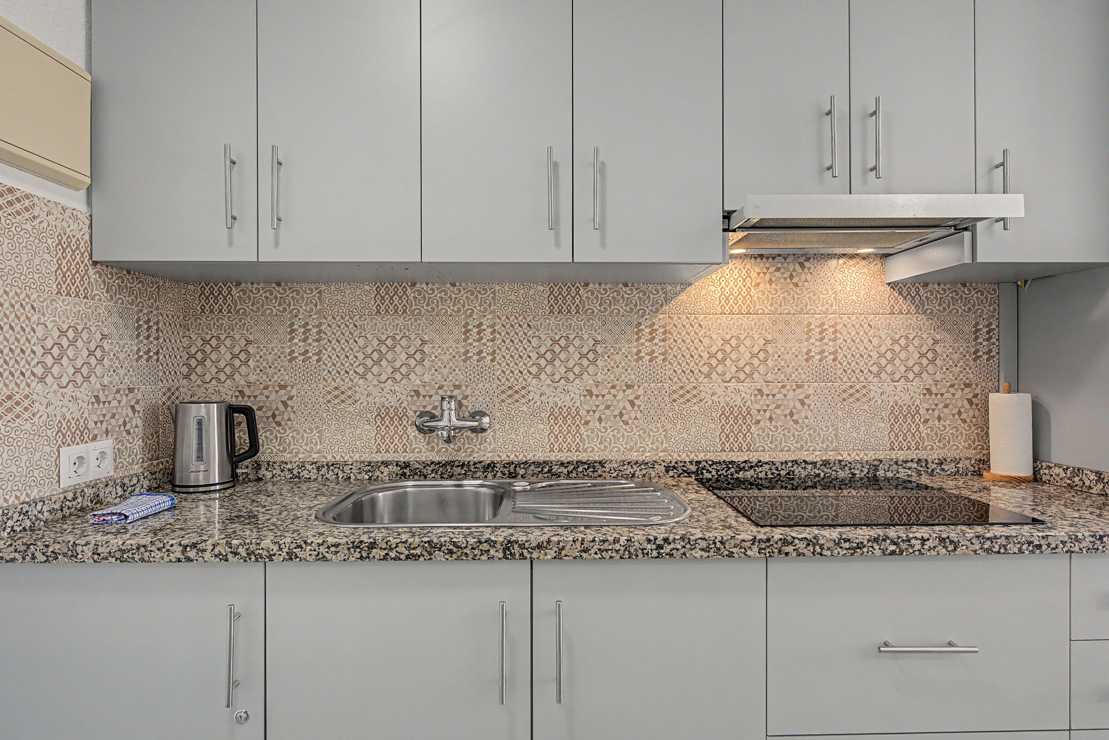 Una cocina con un lavamanos de acero inoxidable, una tetera y azulejos decorativos en la pared.