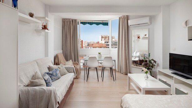 Une chambre d’hôtel moderne équipée d’un canapé, d’une table à manger, de chaises, d’un téléviseur et d’une fenêtre donnant sur la ville.