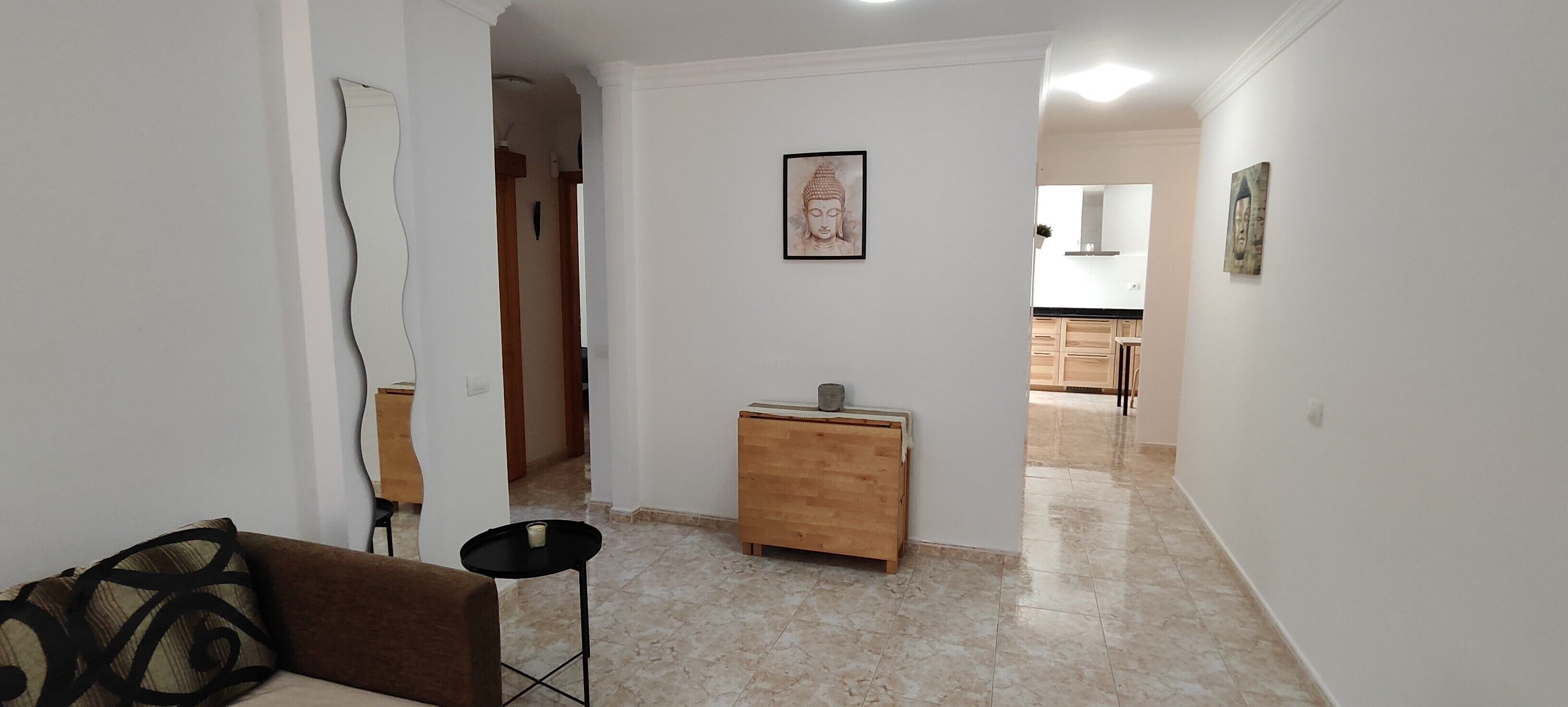 Ein Flur mit einer Couch, einem kleinen Tisch, einem Holzschrank und einer Buddha-Statue an der Wand.