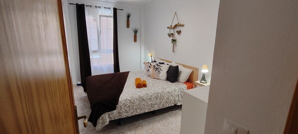 Un dormitorio con cama, mesita de noche con lámpara, ventana con cortinas y decoración en la pared.