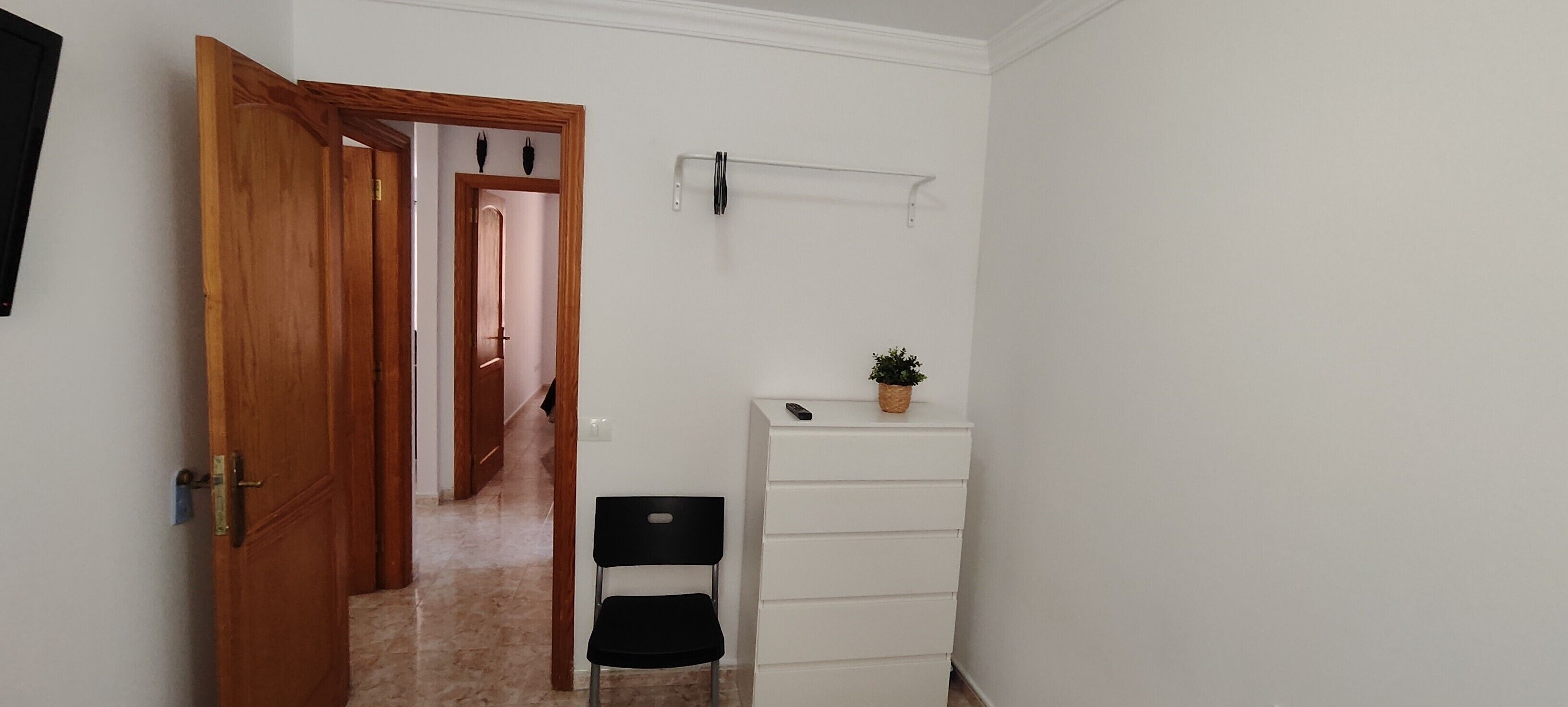 Ein Flur mit einer Holztür, einer weißen Wand, einem schwarzen Stuhl, einem weißen Schrank und einer Pflanze.