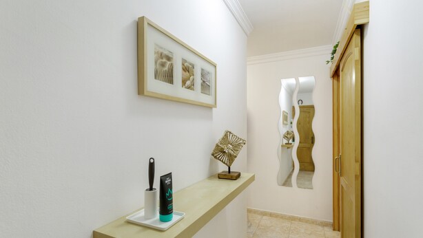 A hallway with a framed artwork, a small table with a knife and a tube, and a wooden door.