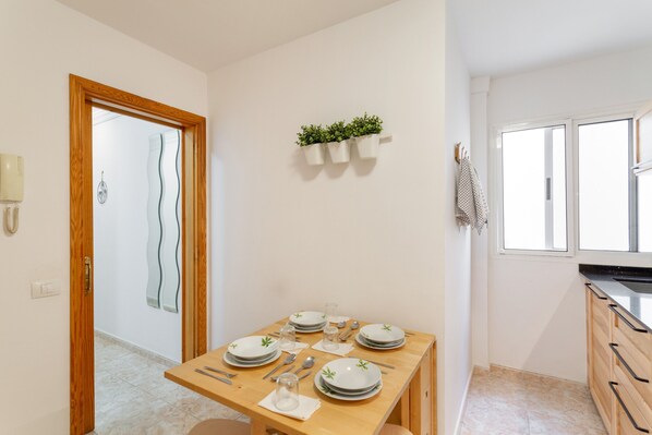 Ein Essbereich mit Holztisch, gedeckt für vier Personen, eine Küche mit Holzschränken und ein Fenster mit Jalousien.