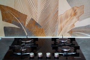 Una cocina con estufa a gas y una pared decorada con motivos abstractos de hojas.