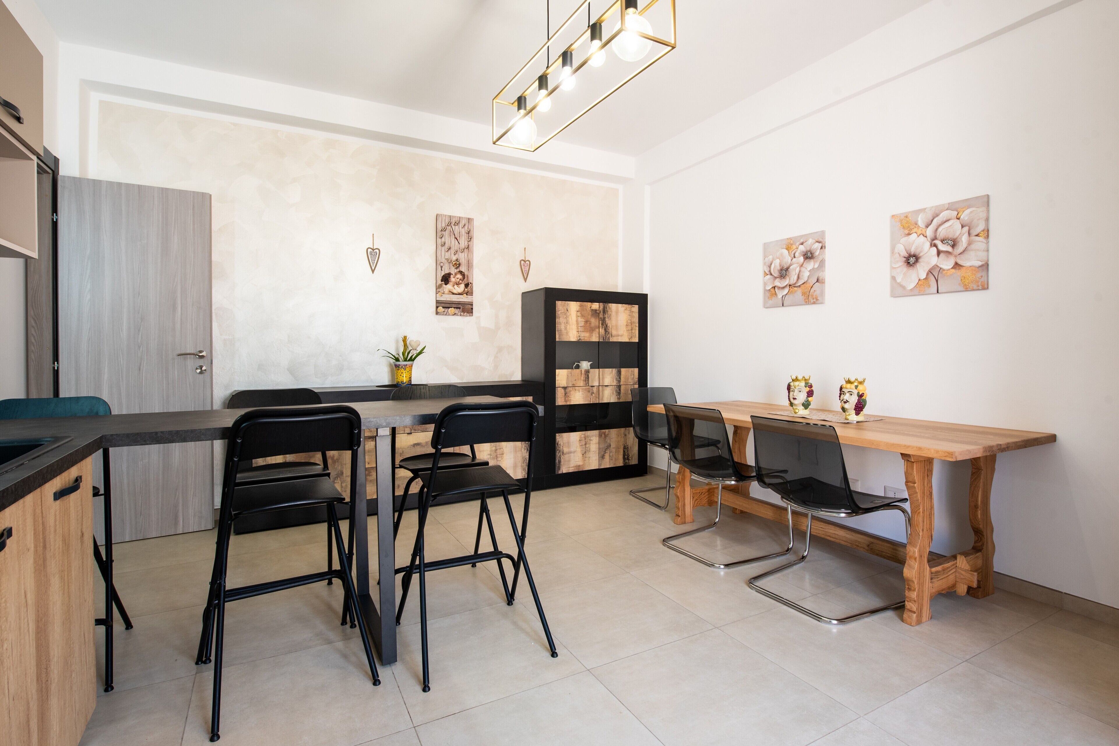 Une cuisine moderne avec une table en bois, des chaises noires, un meuble noir et un luminaire décoratif.