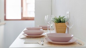 Une table à manger avec des bols roses et des verres à vin, un buffet en bois et une plante en arrière-plan.
