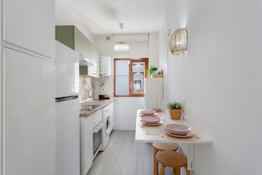 A compact kitchen with a washing machine, a dining area with pink plates, and a wooden table. - Vacation Apartment 'Martimar Candelaria' with Sea View, Shared Pool and Wi-Fi (Candelaria)