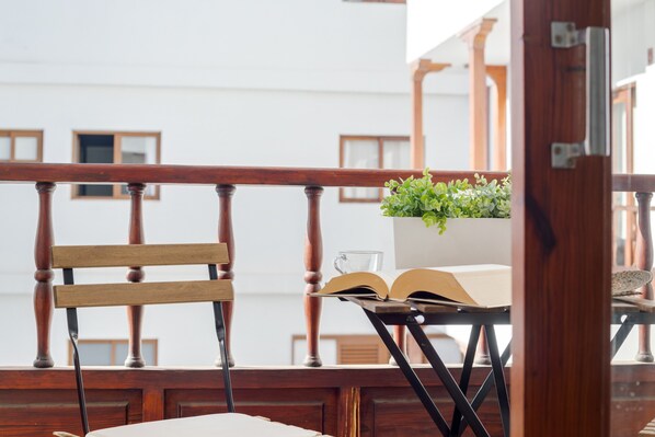A balcony with a wooden chair, a table with an open book and a glass, and a potted plant.