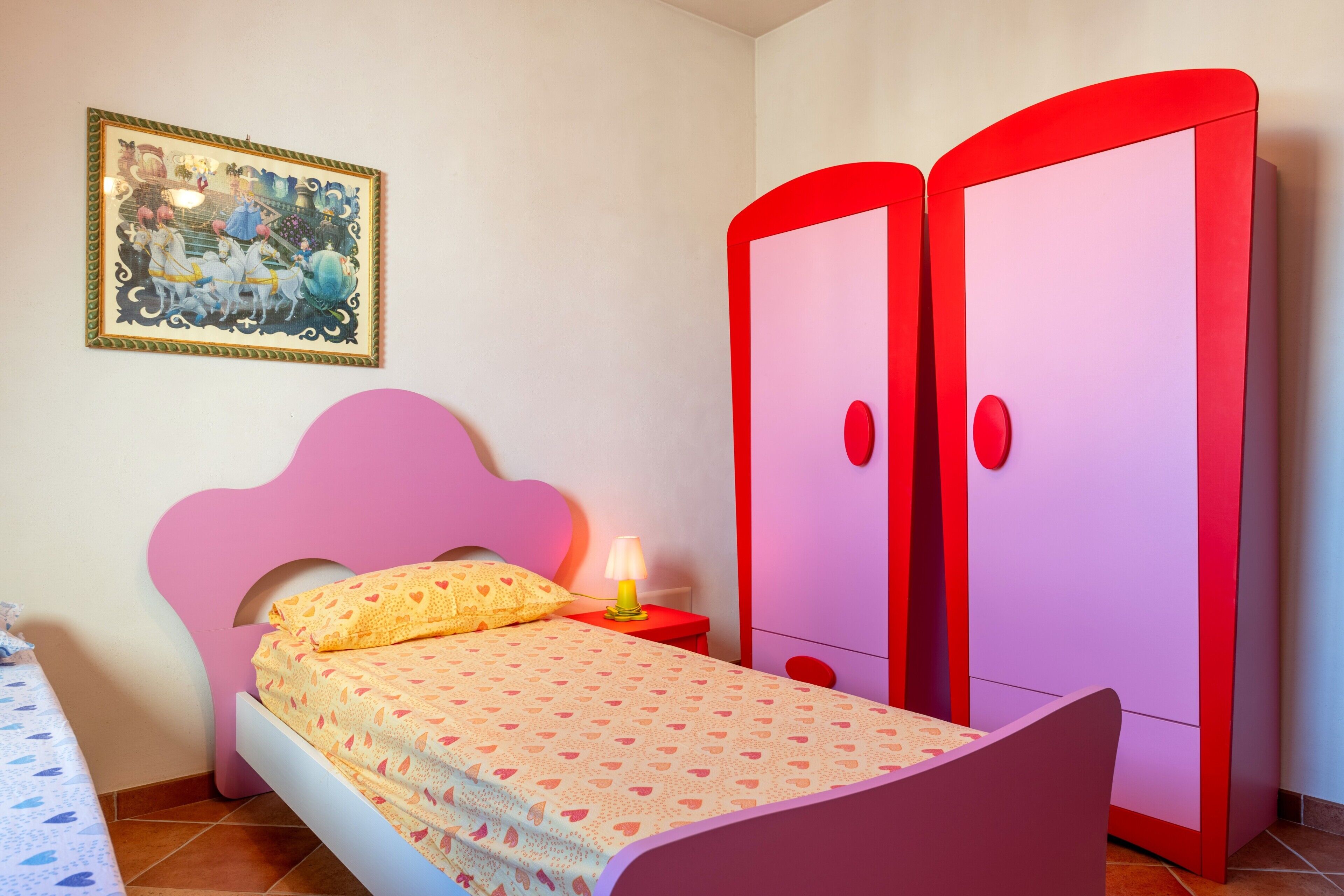 Una camera da letto con un letto, un comodino, una lampada, un armadio e un quadro appeso al muro.