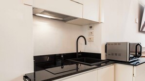 Cocina compacta con encimera negra, pileta integrada, microondas y campana extractora.
