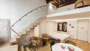 Un interior moderno con una escalera curva, una cama tipo altillo y un comedor con dos sillas y una mesa.