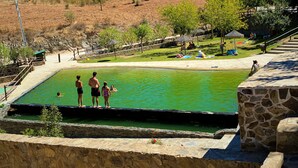 A swimming pool with a stone wall, a grassy area with trees, and a clear blue sky. - Holiday Home 'Casa Moinho Da Eira' with Mountain View, Wi-Fi and Air Conditioning (Loulé)