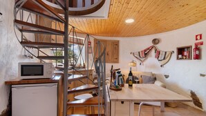 A kitchen with a spiral staircase, a microwave, a refrigerator, a wooden table, and a sofa. - Holiday Home 'Casa Moinho Da Eira' with Mountain View, Wi-Fi and Air Conditioning (Loulé)