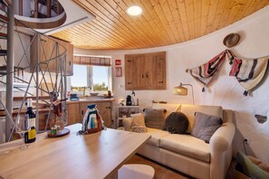 En hyggelig indretning med træloft, hvid sofa, spisebord og et køkken.