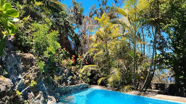 Ein klares, blaues Schwimmbecken, umgeben von üppiger Vegetation und felsigem Gelände.