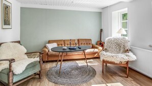 Una sala de estar acogedora con un sofá verde, una mesa de centro redonda, un sillón mullido y una guitarra apoyada en la pared.