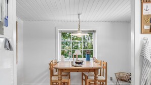 Un comedor con mesa y sillas de madera, una ventana con vista a follaje y una lámpara colgante.