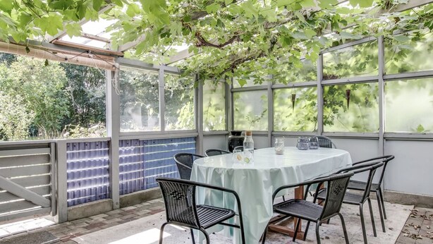 Un porche cubierto con una mesa y sillas, ventanas amplias y vistas a árboles.