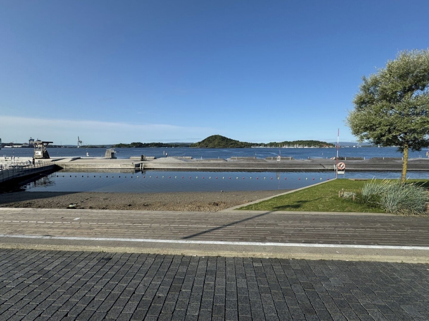 Een waterkantpromenade met een houten looppad, een gazon en een helder uitzicht op het water.