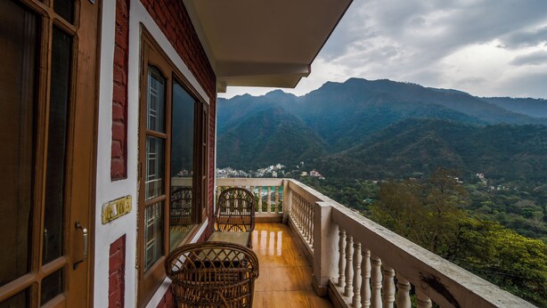 A balcony with a view of mountains, a wooden table, and wicker chairs.