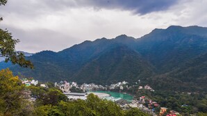 A mountainous landscape with a river, buildings, and dense greenery.