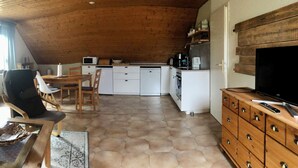 Ett mysigt kök med träpanel i taket, vita skåp och en matplats med bord och stolar.