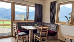 A cozy dining area with a wooden table and chairs, a bench, and large windows offering mountain views.