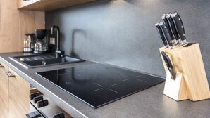 A modern kitchen with a black induction cooktop, wooden cabinets, and a knife block.