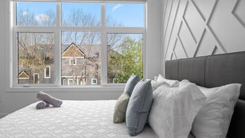Une chambre avec une grande fenêtre, un lit avec des oreillers et une vue sur une maison.