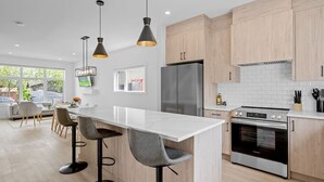 A modern kitchen with a central island, bar stools, a refrigerator, an oven, and pendant lighting.