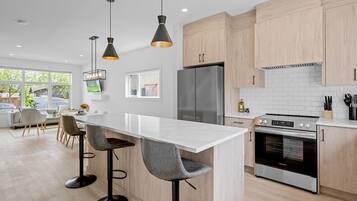Une cuisine moderne dotée d’un îlot central, de tabourets de bar, d’un réfrigérateur, d’un four et de luminaires suspendus.