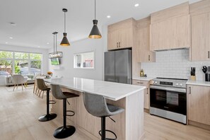Cozinha moderna com ilha central, banquetas, geladeira, forno e iluminação pendente.