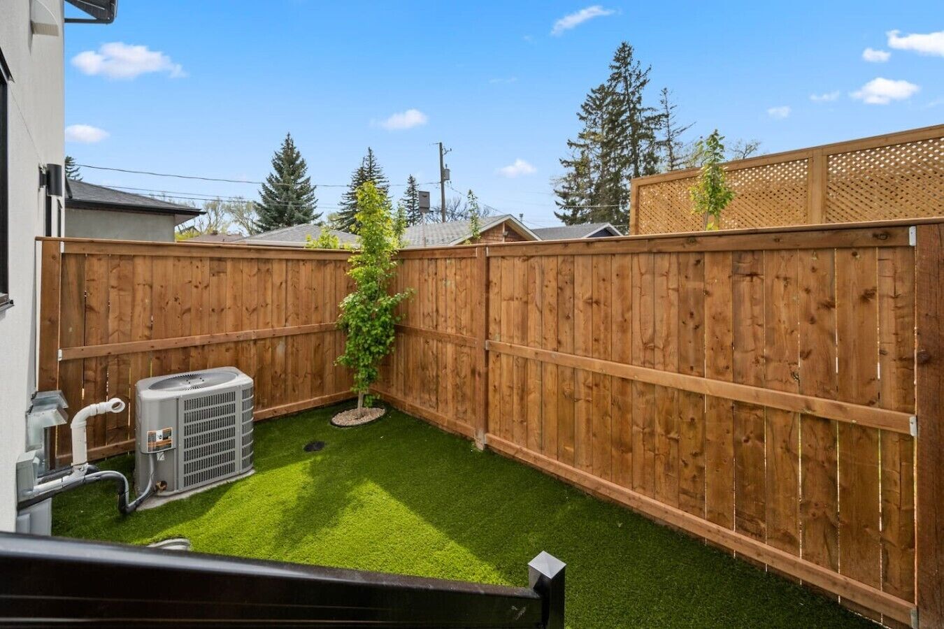 Un jardin avec une pelouse artificielle, une clôture en bois et un appareil de climatisation.