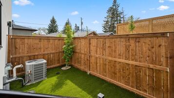 Un jardin avec une pelouse artificielle, une clôture en bois et un appareil de climatisation.