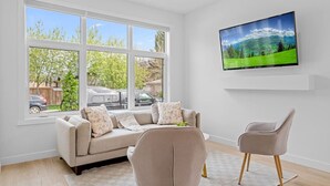 A living room with a sofa, armchair, and a TV on the wall.
