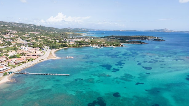 An aerial view of a coastal town with clear turquoise waters, a pier, and buildings along the shoreline.