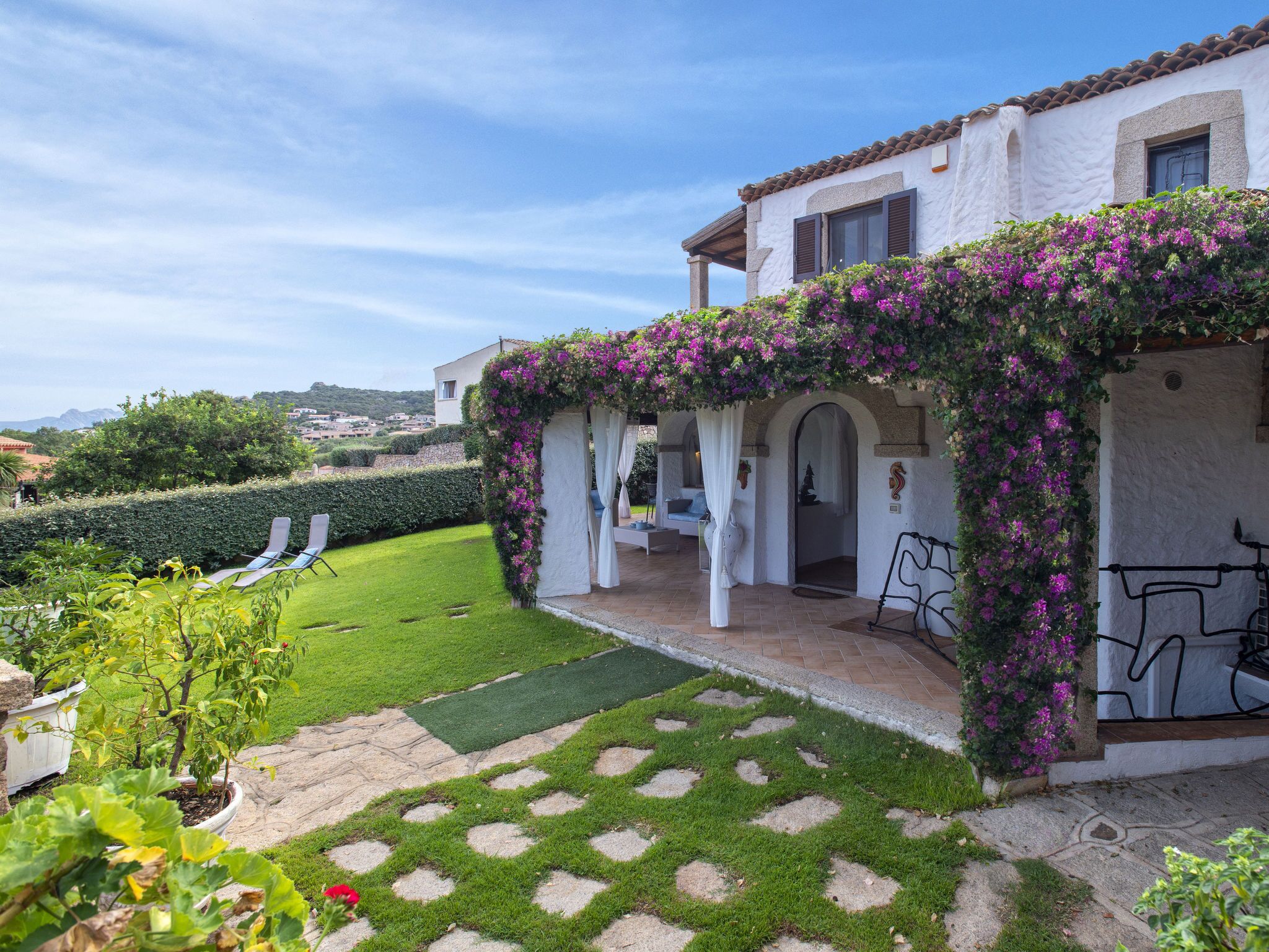 Una villa con jardín, una pérgola cubierta de flores moradas y vistas al campo.